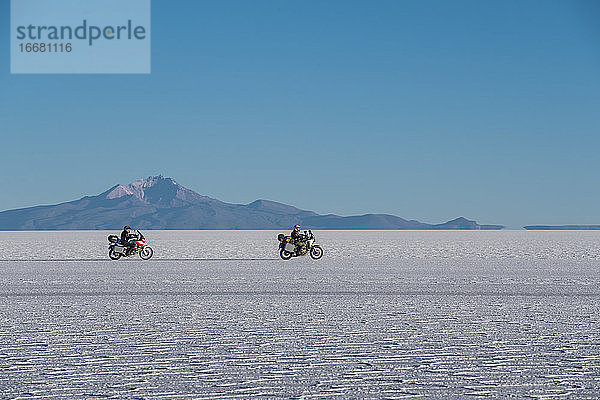 Zwei Männer fahren mit dem Motorrad über die Salinen von Uyuni