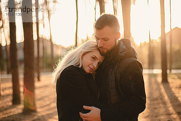 Junges glückliches Paar in der Liebe romantisch stehend im Park bei Sonnenuntergang