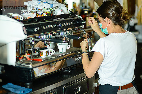 Junge erwachsene kaukasische Barista-Frau mit chirurgischer Gesichtsmaske