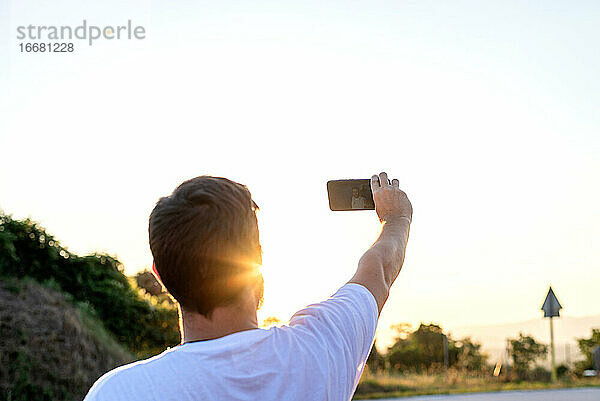 Porträt von hinten eines Mannes  der bei Sonnenuntergang ein Selfie macht