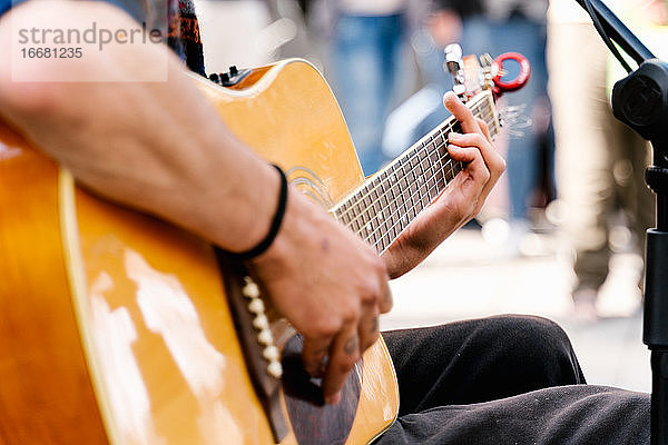 Selektiver Fokus auf die Hände eines jungen Mannes  der auf einer belebten Straße Gitarre spielt