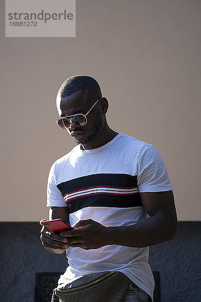 Mann mit Sonnenbrille  der ein Mobiltelefon benutzt.