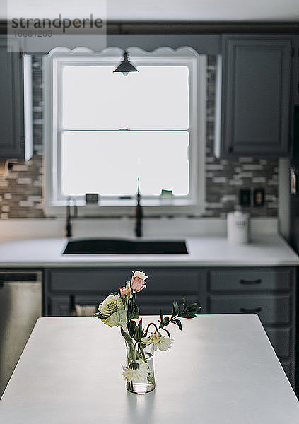 weiße Küchenarbeitsplatte mit Blumen und Vase und Fenster im Hintergrund
