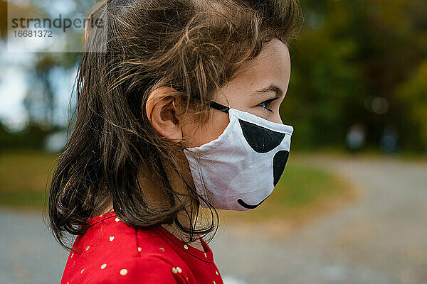 Mädchen im Vorschulalter trägt im Herbst draußen einen Gesichtsschutz