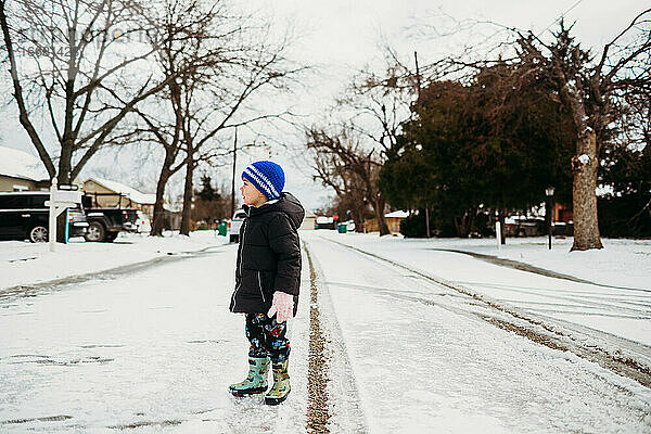 Junge steht auf verschneiter Straße und trägt eine Jacke im Winter