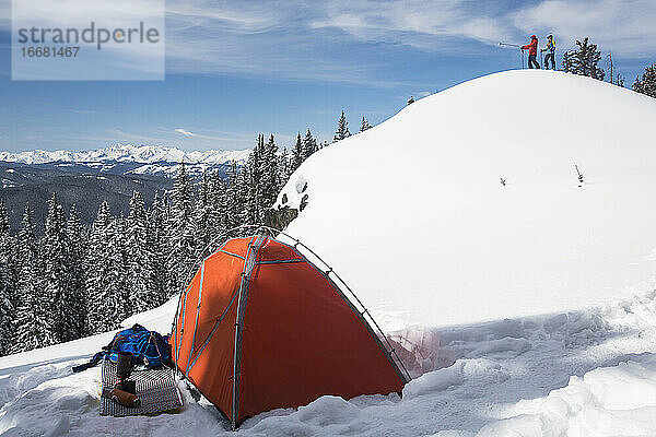 Männlicher und weiblicher Wanderer stehen auf einem schneebedeckten Berg mit einem Zelt im Vordergrund