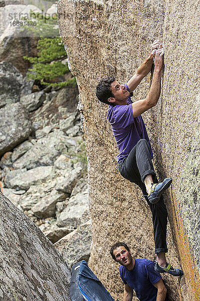 Sportlicher Mann klettert draußen auf einem Felsbrocken mit männlichem Beobachter