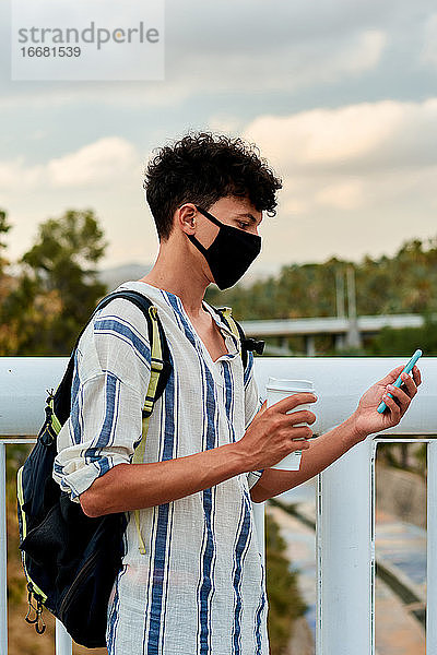 Junger Afro-Mann mit Maske benutzt sein Handy auf der Straße