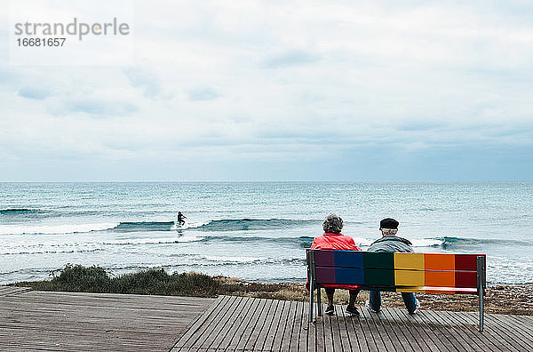 Ein altes Paar  das auf einer bunten Bank sitzt und aufs Meer hinausschaut
