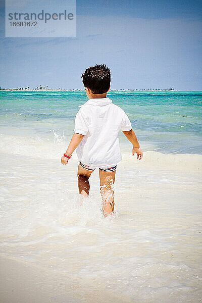 Kleiner Junge geht am Strand spazieren und beobachtet das karibische Meer