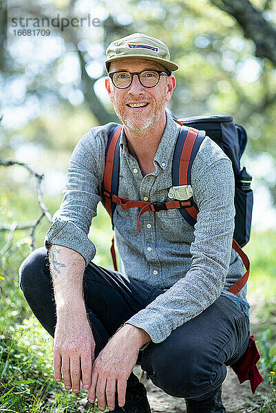 Porträt eines Rucksacktouristen  der auf einem Wanderweg kniet und lächelt  in Kalifornien