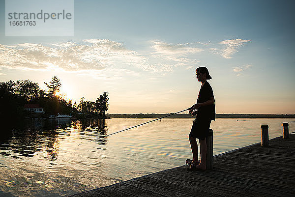 Heranwachsender Junge beim Angeln am Steg eines Sees bei Sonnenuntergang in Ontario  Kanada.