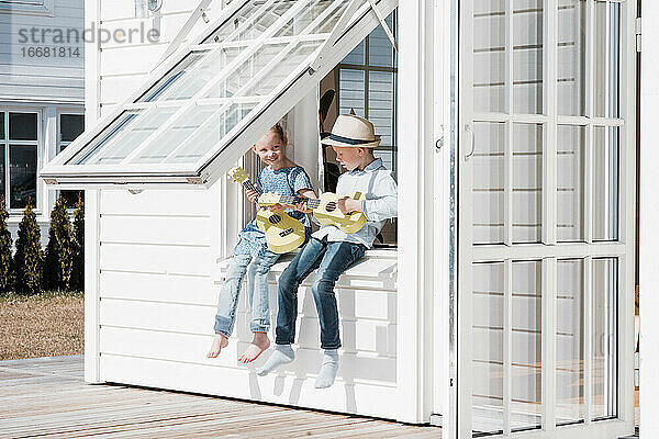 Bruder und Schwester saßen zu Hause am Fenster und spielten zusammen Gitarre