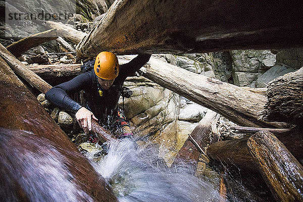 Mann  der eine Schlucht erkundet  klettert durch einen Baumstamm  trägt Helm und Neoprenanzug