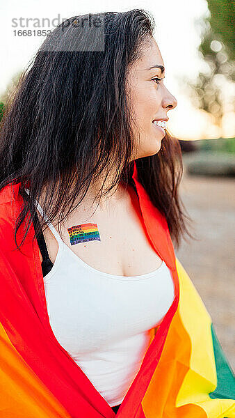 Glückliche Frau mit einer IGB-Flagge und einem Gay-Pride-Tattoo auf der Brust