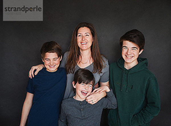 Mutter mit drei älteren Jungen  die vor einem schwarzen Hintergrund lachen.