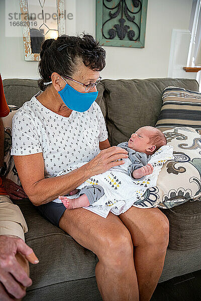 Frau mit Gesichtsmaske hält neugeborenes Baby.