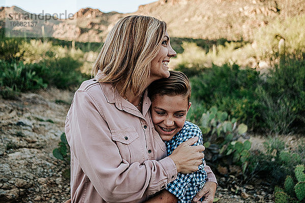 Mutter umarmt lächelndes nicht-binäres Kind in der Wüste
