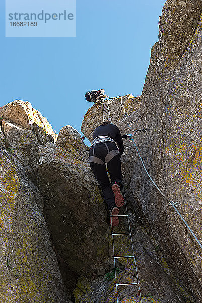 Konzept: Abenteuer. Bergsteigerin mit Helm und Klettergurt. Klettern auf einer Eisenleiter  die in der natürlichen Wand verankert ist. Via ferrata in den Bergen.