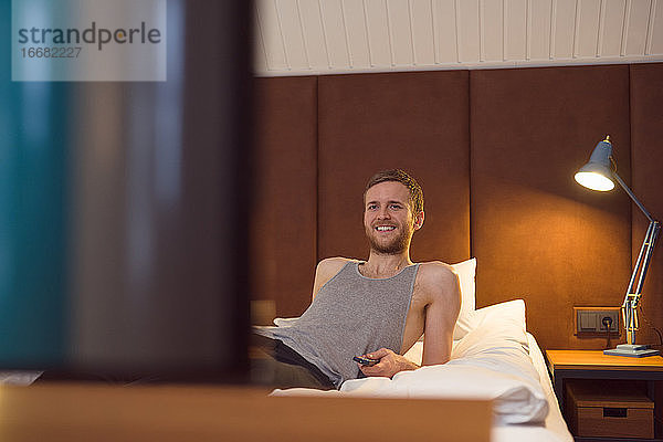 Glücklicher Mann sieht auf dem Bett fern