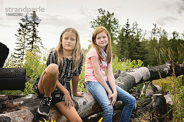 Zwei junge Mädchen  die auf einem Baumstamm sitzen