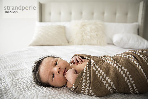 Neugeborenes Baby mit vielen dunklen Haaren liegt gewickelt auf dem Bett zu Hause