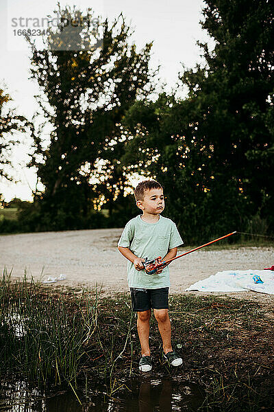 Junger Junge steht draußen am See und hält eine Angelrute