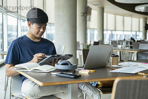 Junger Collegestudent mit Computer und mobilem Gerät beim Lernen