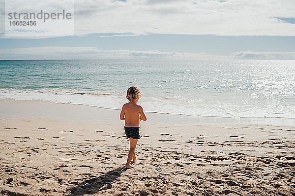 Junge  der an einem sonnigen Tag im Urlaub am Strand ins Wasser geht