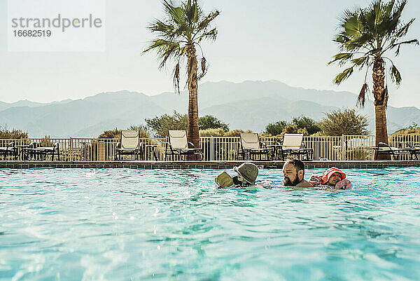 Vater und kleine Kinder schwimmen im großen kalifornischen Pool im Urlaub