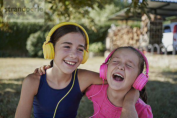 Kleine Mädchen hören Musik und lächeln mit gelben und rosa Kopfhörer in einem Garten. Glück Konzept