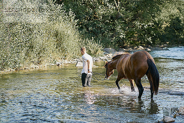 Porträt eines jungen blonden Mannes  der auf einem Pferd über einen Fluss reitet