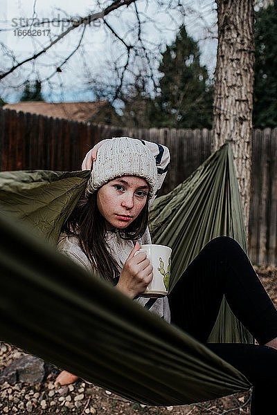 Vertikales Porträt von Teenager-Mädchen entspannt in Hängematte mit Kaffeebecher