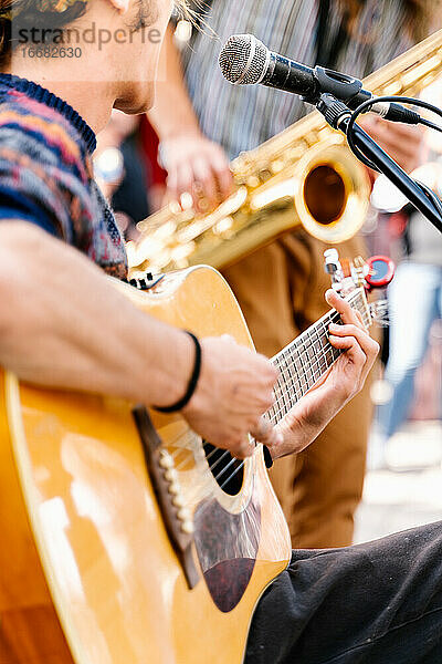 Selektiver Fokus auf die Hände eines jungen Mannes  der auf der Straße eine Gitarre spielt