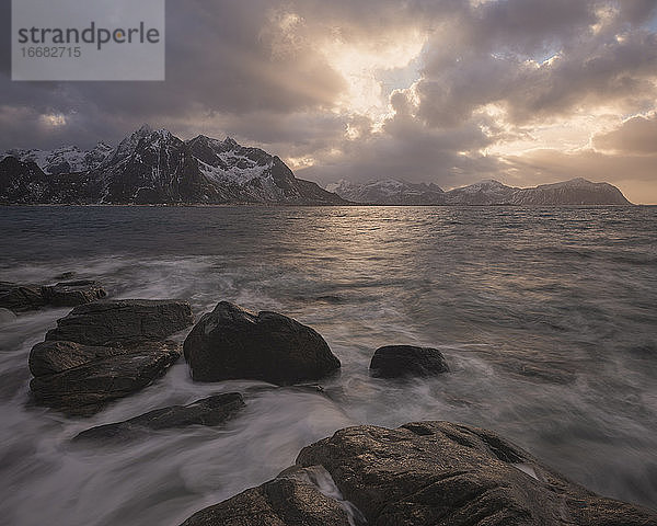 Die schroffen Berge von Flakstadøy erheben sich vor der felsigen Küste von Vareid  Lofoten  Norwegen  über das Meer.