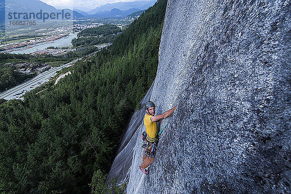 Mann beim Klettern am Squamish Chief mit Blick auf die Kamera im Stadthintergrund