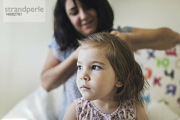4 Jahre altes Mädchen mit großen braunen Augen und lächelnder Mutter  die ihr Haar flechtet