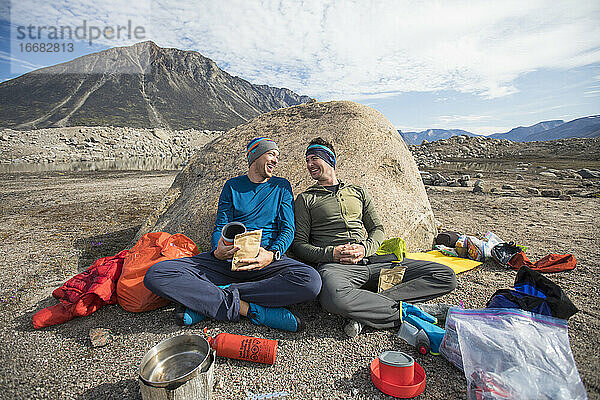 Kletterpartner lachen gemeinsam beim Essen auf dem Zeltplatz.