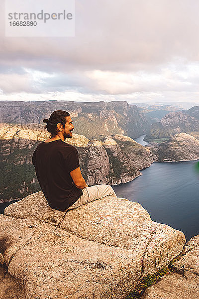 Mann sitzt lächelnd in einem Felsen am Rande einer Klippe am Preikestolen  Norwegen