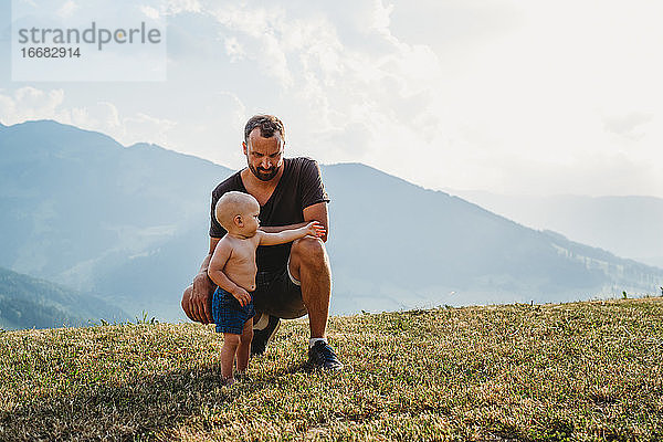 Weißer Vater kniend und Baby Junge in den Bergen mit Sonnenuntergang Licht