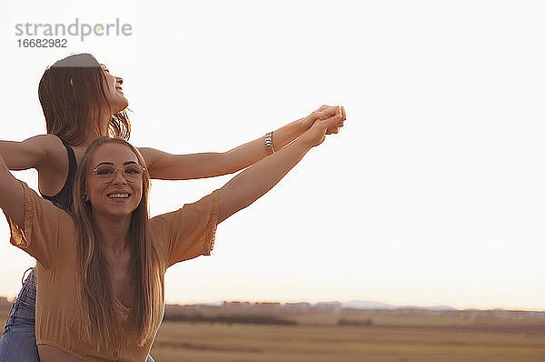 zwei Frauen halten sich bei Sonnenuntergang auf einem Feld an den Händen