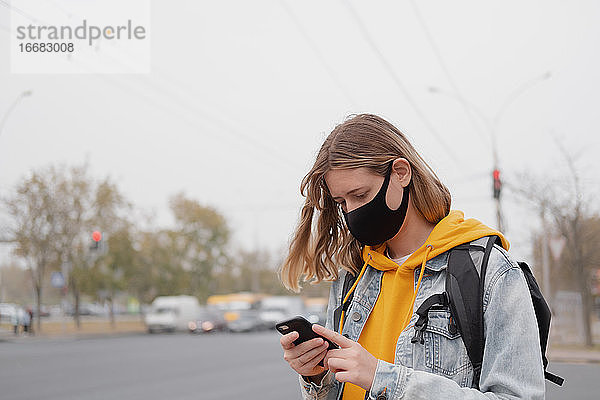 Porträt einer Frau mit Maske und Smartphone. Draußen im Freien sein