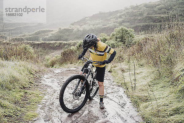 Ganzkörper-Radfahrerin auf schlammigem Bergpfad an einem regnerischen Tag