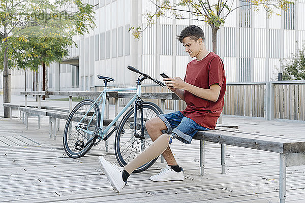 Mann mit Behinderung benutzt Smartphone in der Nähe des Fahrrads