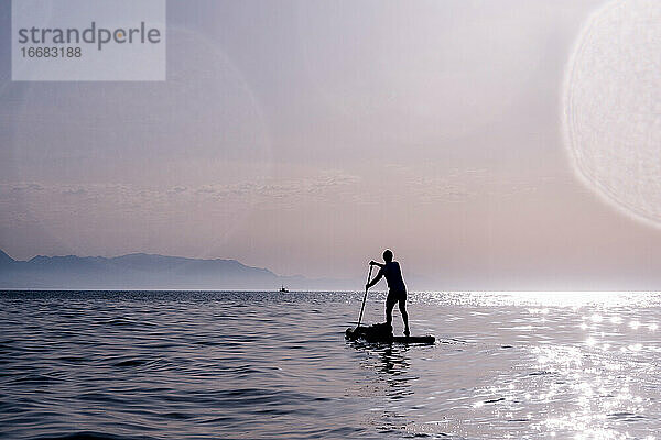 Silhouette eines Mannes  der Stand Up Paddle spielt. Paddeln auf dem Meer in der Morgendämmerung.