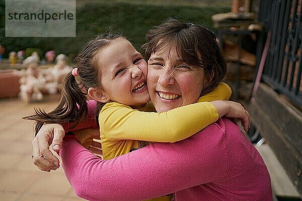 Seitenansicht einer fröhlichen Frau  die ihre Tochter umarmt und sich auf einer Bank ausruht