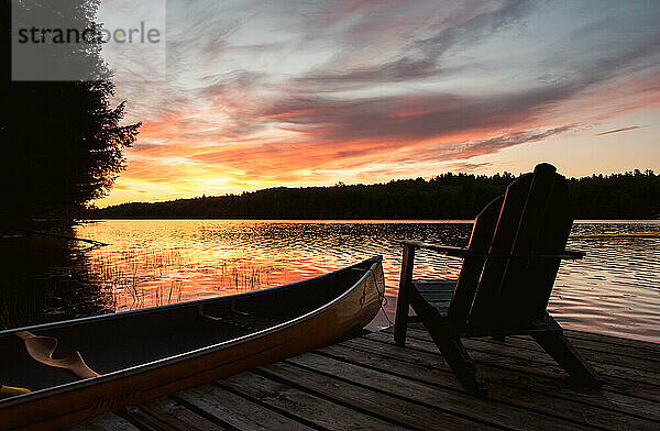 Kanu und Adirondack-Stuhl auf einem Steg an einem See bei Sonnenaufgang.
