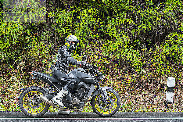 Frau hält ihr Motorrad am Straßenrand in Thailand an
