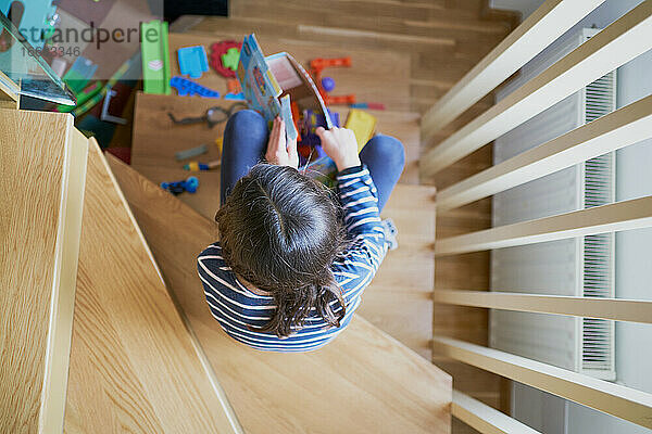 Von oben anonymes Mädchen  das auf den Stufen sitzt und zu Hause mit Spielzeug spielt