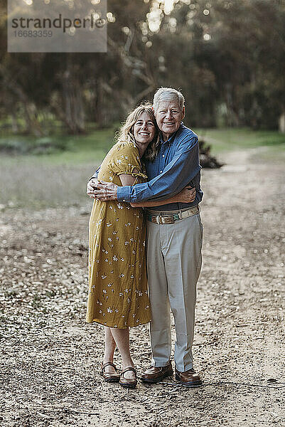 Porträt einer erwachsenen Frau und eines älteren Vaters  die sich im Park umarmen